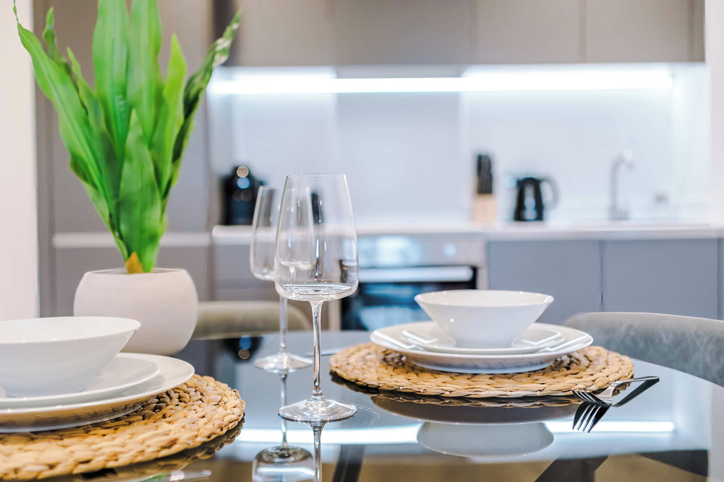 A dining table set with white plates, bowls, and a glass of water, with a woven placemat and a fork on the right.