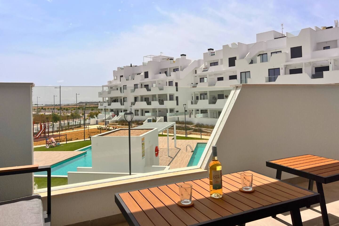 A balcony with a pool, outdoor seating, and a view of a modern building complex.