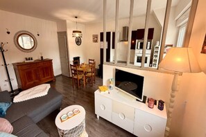 A living room with a sofa, a dining table with chairs, a TV stand with a TV, and a lamp. - Bright apartment with mountain view (Mont-Dore)
