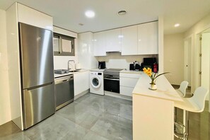 A modern kitchen with stainless steel appliances, a washing machine, and a dining area with a white countertop and chairs. - Casa Nieve by Rental Hero (Alcazares, Los)
