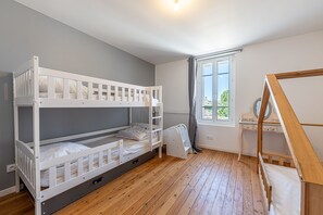 Ein Zimmer mit einem Etagenbett, einem Schreibtisch mit Stuhl, einem Fenster mit Vorhängen und einem Heizkörper.