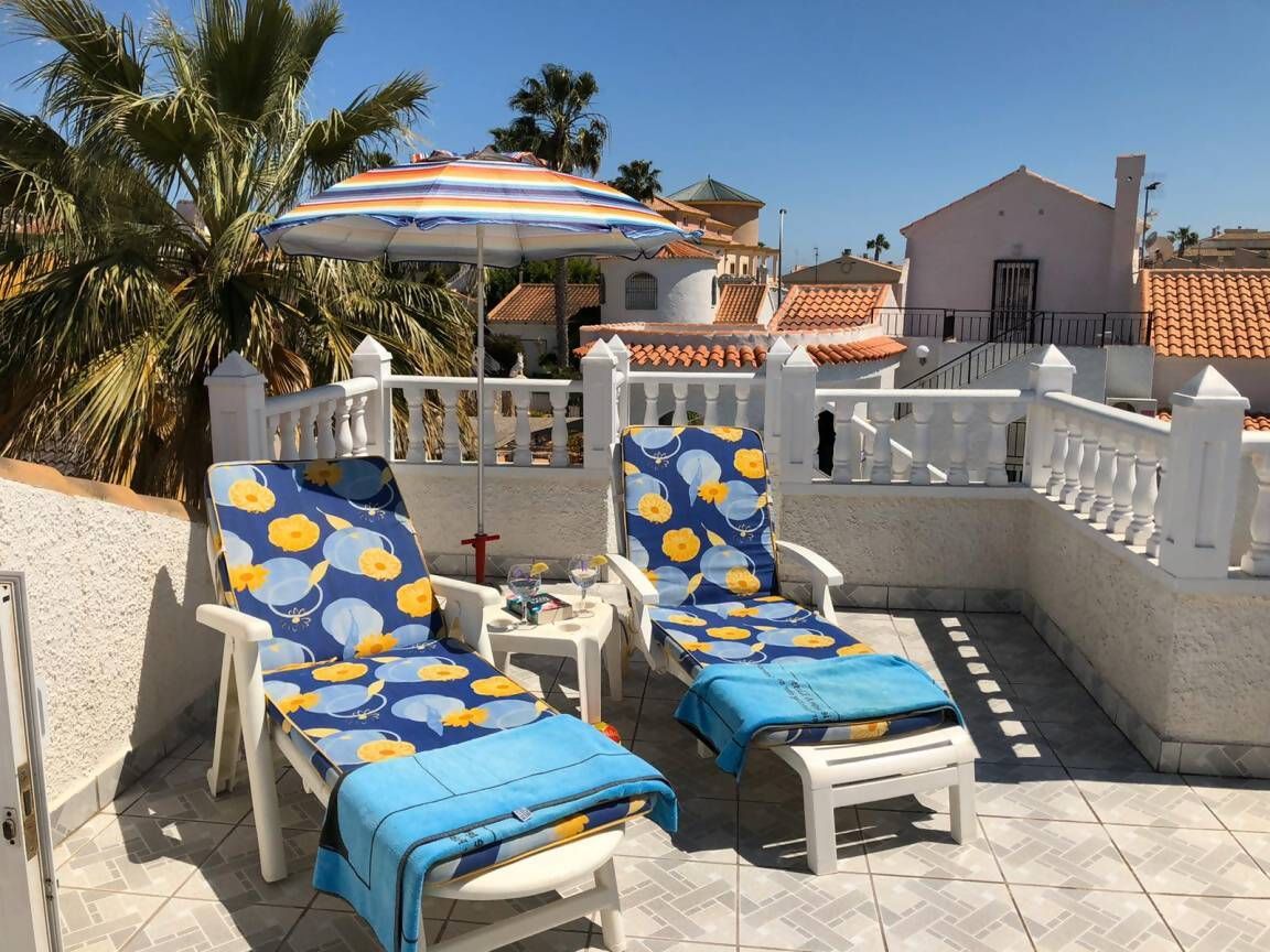 Eine Terrasse mit zwei Liegestühlen, einem Tisch, einem Glas und einem Zierteil-Sonnenschirm.