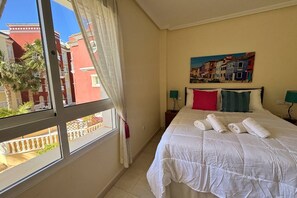 A hotel room with a bed, a painting, a window with curtains, and a view of buildings outside. - Casa Pool Paradise by Rental Hero (Alcazares, Los)