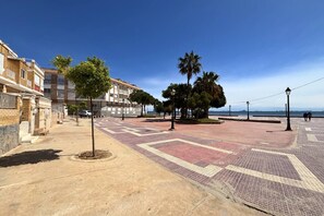 A paved walkway with trees and a building complex in the background. - Casa Playa Espejo by Rental Hero (Alcazares, Los)