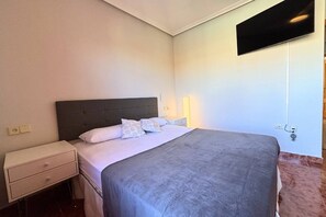 A hotel room with a bed, bedside table, lamp, and a television mounted on the wall. - Casa Rio Sena by Rental Hero (San Pedro Del Pinatar)