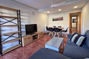 A living room with a TV, sofa, coffee table, and a dining area with chairs and a table. - Casa Rio Sena by Rental Hero (San Pedro Del Pinatar)