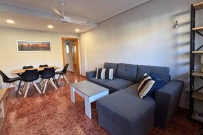 Un salon avec un canapé gris, une table basse et un coin repas comprenant des chaises et une table.