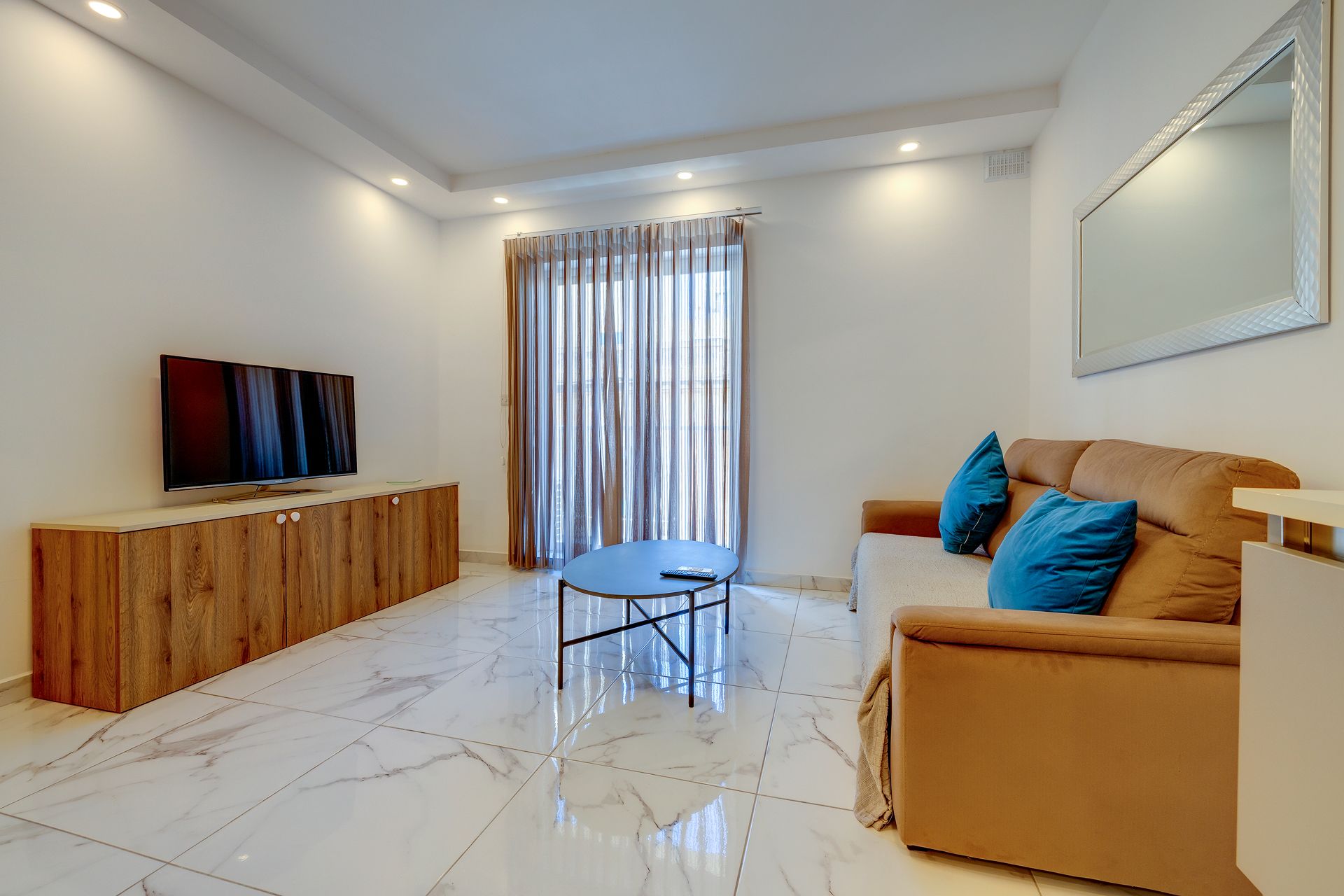 Una sala de estar moderna con un televisor de pantalla plana, un mueble de madera, una mesa azul, un sofá marrón con cojines azules y un ventanal con cortinas.