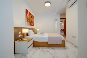 A modern hotel room with a wooden bed, white bedding, a bedside table with a lamp, and a painting on the wall. - Stylish 2BR Getaway Steps From the Promenade (Gzira)