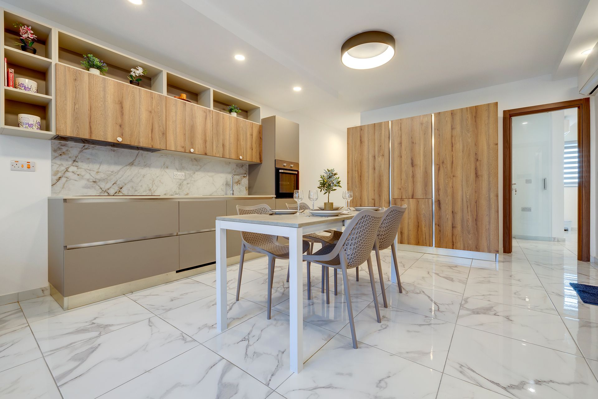 Una cocina moderna con armarios de madera, encimera de mármol y un comedor con mesa blanca y sillas de mimbre.
