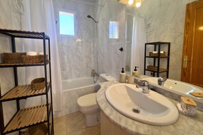 A bathroom with a bathtub, toilet, and a large mirror. There are wicker baskets on shelves and a wooden door. - Casa Caroli by Rental Hero (Narejos, Los)