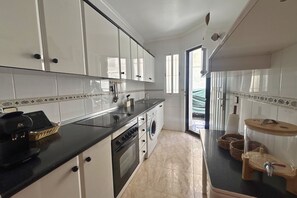 A kitchen with white cabinets, a black countertop, a washing machine, and a small sink. - Casa Caroli by Rental Hero (Narejos, Los)
