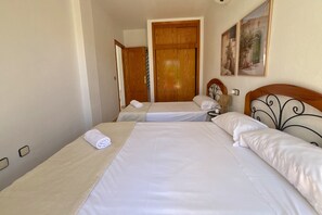 Una habitació d'hotel amb dos llits, una porta de fusta, una tauleta de nit i una làmpada penjada a la paret.