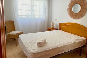 Une chambre à coucher avec un lit, une chaise, une table de chevet avec une lampe et une fenêtre avec des rideaux.