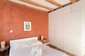 A bedroom with a bed, a nightstand, a lamp, a framed picture on the wall, and a wardrobe. - Le Macareux - Duplex pour 4 (Saint-Malo)