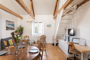 A dining area with a wooden table, chairs, and a view of a staircase. - Le Macareux - Duplex pour 4 (Saint-Malo)