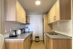 A compact kitchen with wooden cabinets, a microwave, a kettle, and a trash bin. - Casa Elkie by Rental Hero (Torre Pacheco)