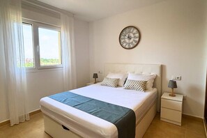 A hotel room with a bed, a bedside table with a lamp, a window with curtains, and a wall clock. - Casa Elkie by Rental Hero (Torre Pacheco)