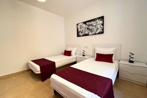 A hotel room with two beds, each with a red accent pillow, a white headboard, and a black abstract painting on the wall. - Casa Elkie by Rental Hero (Torre Pacheco)