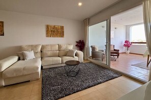 A living room with a beige sofa, a coffee table, and a large sliding glass door leading to an outdoor patio area. - Casa Elkie by Rental Hero (Torre Pacheco)