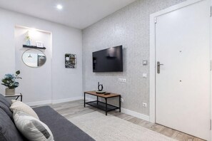 A modern living room with a flat-screen TV mounted on the wall, a small wooden coffee table, a grey sofa, and a white door. - Apartment near Retiro Park (Madrid)
