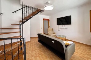 A living room with a staircase, a sofa, a chair, a coffee table, and a flat-screen TV mounted on the wall. - Casa Mare Nostrum by Rental Hero (Alcazares, Los)