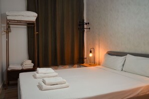 Habitació d'hotel amb un llit, una taula de nit, una làmpada, un escurapins i una cortina.