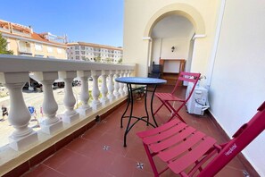 Ein Balkon mit Tisch und Stühlen, ein Fliesenboden und ein Blick auf Gebäude im Hintergrund.