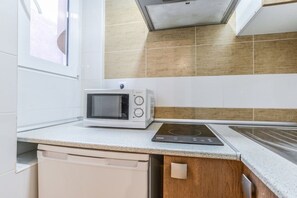Eine Küche mit Mikrowelle, Induktionskochfeld, weißen Schränken und einem Fenster.