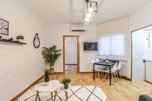 Uma sala de estar moderna com área de jantar, piso de madeira, televisão de tela plana e uma janela grande.