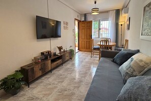 A living room with a sofa, a TV mounted on the wall, a wooden cabinet, and a dining area with a table and chairs. - Casa Cisne by Rental Hero (Alcazares, Los)