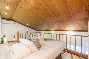 A bedroom with a sloped ceiling, a bed with white bedding, a wooden railing, and a small bedside table with a lamp. - Penthouse with Terrace, Plaza Espana (Madrid)