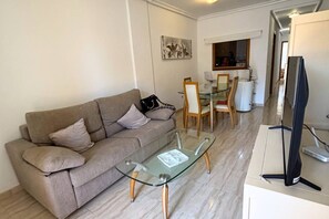 A living room with a glass-top coffee table, a sofa, and a flat-screen TV. - Casa Playa Lo Pagan by Rental Hero (San Pedro Del Pinatar)