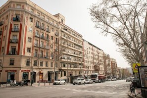 Un immeuble à plusieurs étages doté de balcons, une rue devant et un panneau indiquant une station de taxis.