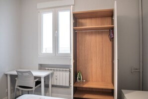 Una habitación con un armario de madera, un escritorio blanco con una silla y un radiador.