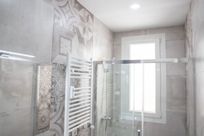 Une salle de bain moderne avec des carreaux à motifs, une douche en verre et une fenêtre qui laisse entrer la lumière naturelle.