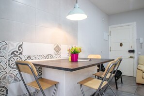 Une cuisine compacte avec un îlot central, deux chaises, un luminaire suspendu et une porte visible au fond.
