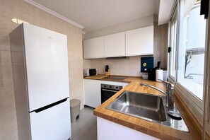 A modern kitchen with white cabinets, a stainless steel sink, and a wooden countertop. - Casa Volvoreta by Rental Hero (Alcazares, Los)