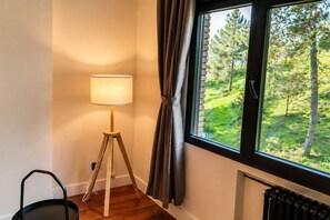 Una habitación con una lámpara de pie, una ventana con cortinas y vistas a un bosque.