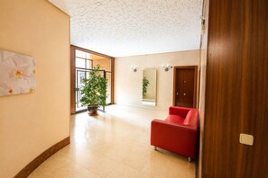 A spacious lobby with a red sofa, a large potted plant, and a wooden door. - Spacious Madrid Apartment with Garden (Madrid)