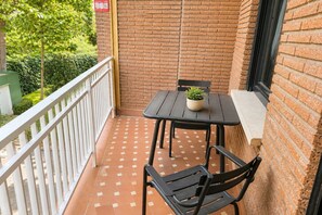 Ein kleiner Balkon mit Sitzgelegenheit, Tisch, Pflanztopf und weißem Geländer.