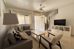 A living room with a sofa, a coffee table, a TV on a stand, and a staircase. - Casa San Juda by Rental Hero (Alcazares, Los)