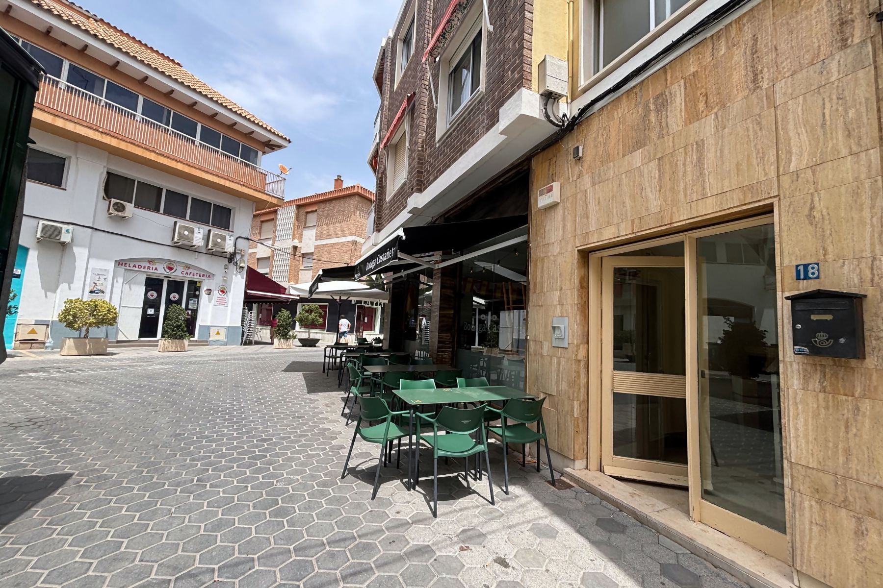 A street with outdoor seating, a cafe, and a building with a large window and a mailbox.