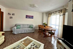 A living room with a sofa, dining table, chairs, a television, and a decorative box. - Casa Du Viño by Rental Hero (Alcazares, Los)