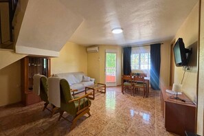 A living room with a sofa, a dining table with chairs, a television mounted on the wall, and a staircase leading to an upper level. - Casa de la Luz by Rental Hero (Alcazares, Los)