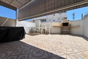 A rooftop patio with a patterned floor, a grill, and a table with chairs. - Casa de la Luz by Rental Hero (Alcazares, Los)