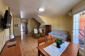 A living room with a sofa, chairs, a dining table, a TV, and a staircase leading to another room. - Casa de la Luz by Rental Hero (Alcazares, Los)
