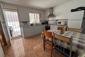 A compact kitchen with a microwave, stove, and a small dining table with chairs. - Casa de la Luz by Rental Hero (Alcazares, Los)