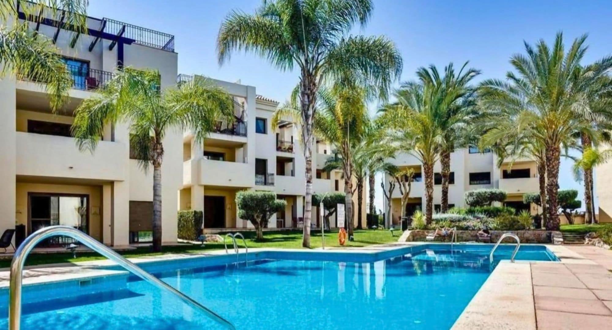 Une piscine entourée de palmiers et un immeuble à plusieurs étages doté de balcons.