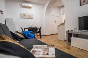 Ein modernes Wohnzimmer mit einer Couch, einem Esstisch und einer Küchenzeile im Hintergrund.